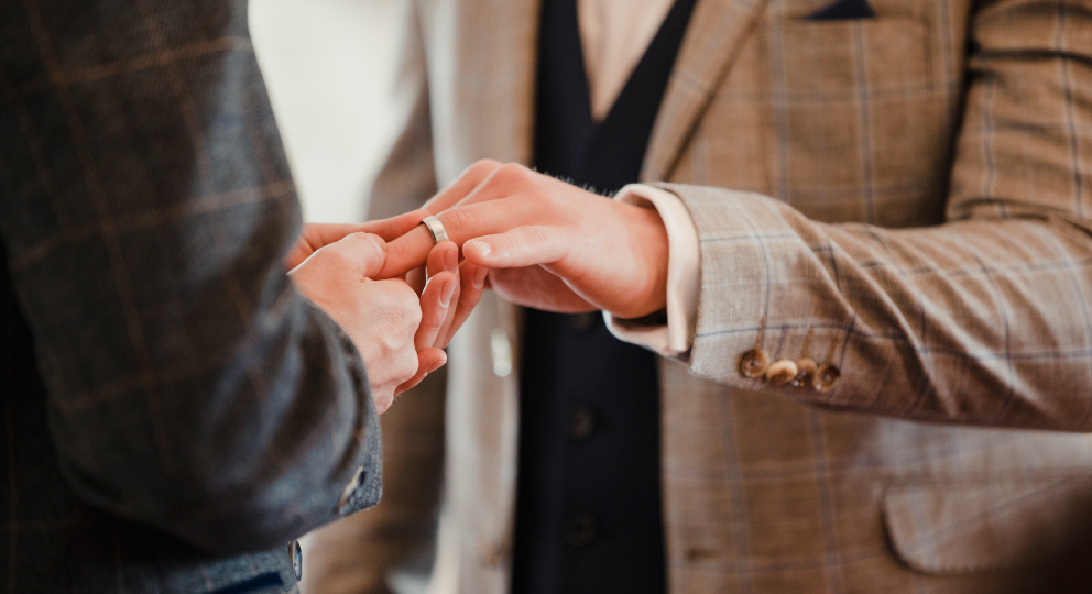 Close-up photo of a person placing a ring on their spouse's hand.