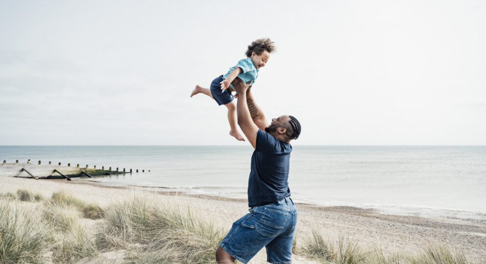 Father playfully throwing son into air on the beach