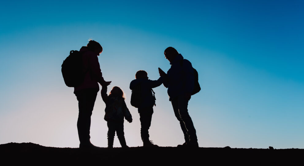 Silhouettes of happy family with two kids hiking at sunset