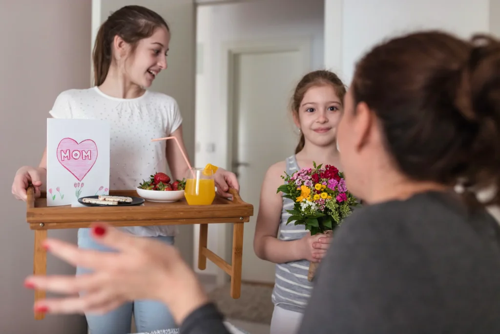 Kids bringing mom breakfast in bed and flowers on Mother's Day.