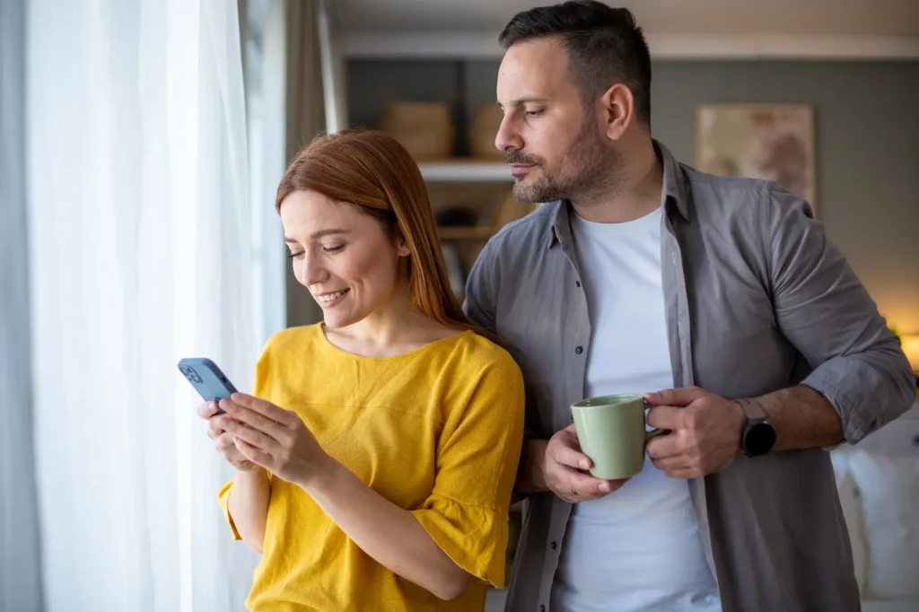 Controlling husband watching his wife on her phone.