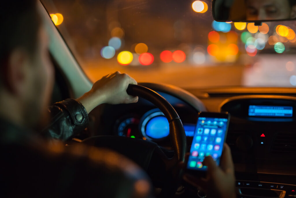 Driver holding a smartphone at the wheel of a car at night.