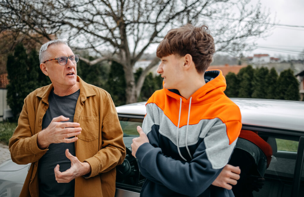 Father and teenage son talking beside a car.