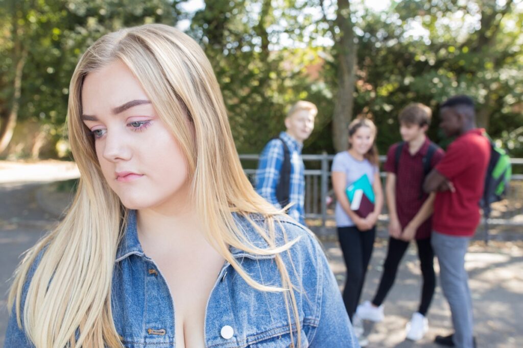 Teenage girl standing apart from a group of peers outdoors.