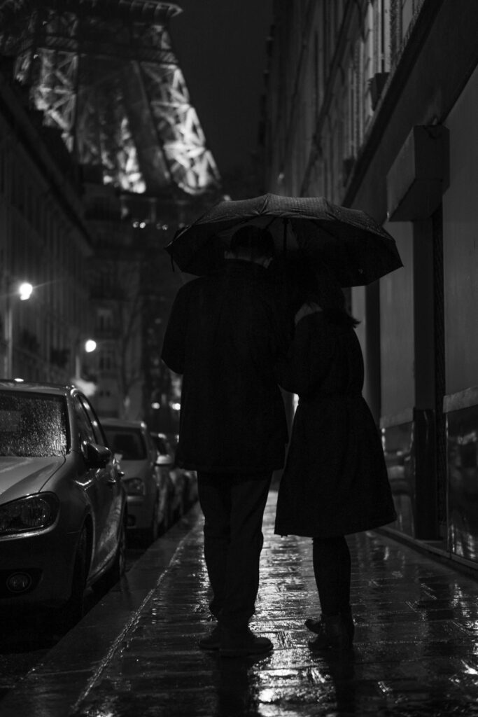 A couple embracing under an umbrella on a rainy street.