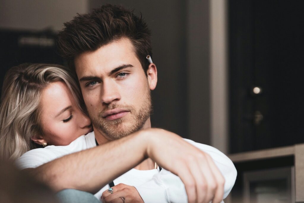 A woman embraces a seated man, resting her face against his cheek.