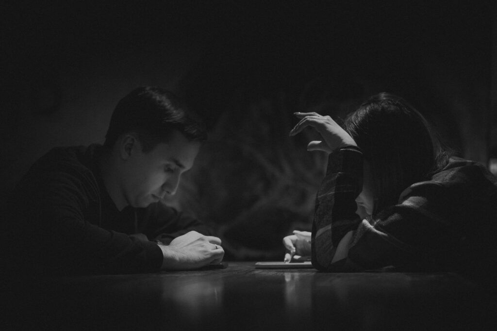 A couple at a dark table, each looking down at a phone, not at each other